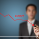 Man behind a graph drawing a line downward that says cost